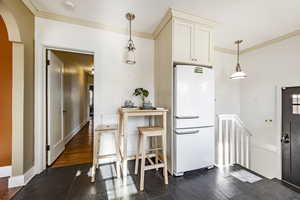 Kitchen with hanging light fixtures, crown molding, and white fridge