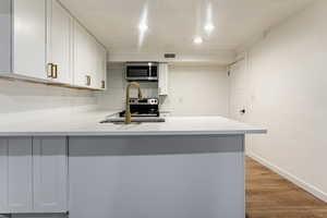 Kitchen with light hardwood / wood-style floors, sink, white cabinetry, and kitchen peninsula