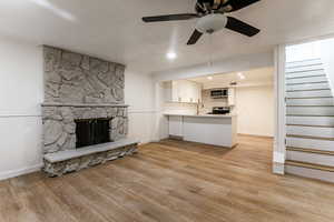 Unfurnished living room with light wood-type flooring, ceiling fan, a stone fireplace, and sink