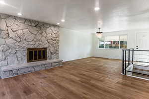 Unfurnished living room featuring a fireplace, an inviting chandelier, a textured ceiling, and dark hardwood / wood-style floors