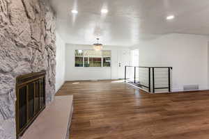 Unfurnished living room featuring a chandelier, dark hardwood / wood-style flooring, and a stone fireplace