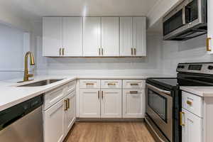 Kitchen with decorative backsplash, sink, white cabinetry, light wood-type flooring, and stainless steel appliances