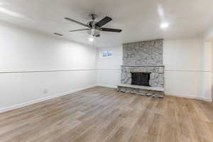 Unfurnished living room featuring a textured ceiling, ceiling fan, light hardwood / wood-style floors, and a stone fireplace