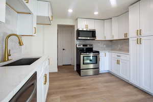 Kitchen with sink, light wood-type flooring, light stone countertops, appliances with stainless steel finishes, and white cabinets