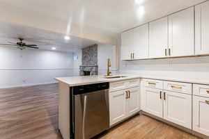 Kitchen with stainless steel dishwasher, kitchen peninsula, sink, and white cabinetry