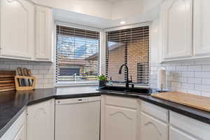 Kitchen featuring tasteful backsplash, white cabinets, dishwasher, and sink