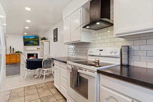 Kitchen featuring white cabinetry, wall chimney range hood, white electric range oven, and tasteful backsplash