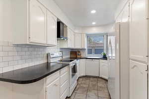 Kitchen featuring white cabinetry, white appliances, and wall chimney exhaust hood