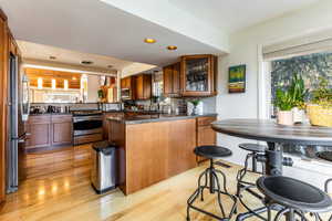 Kitchen featuring appliances with stainless steel finishes, light hardwood / wood-style floors, kitchen peninsula, sink, and tasteful backsplash