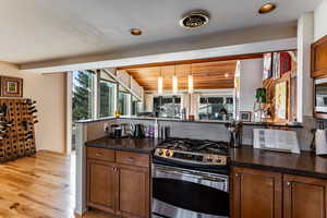 Kitchen with dark stone counters, light wood-type flooring, stainless steel range with gas cooktop, and tasteful backsplash