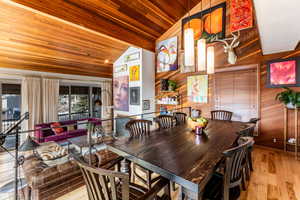 Dining room featuring wood ceiling, light wood-type flooring, wooden walls, and vaulted ceiling with beams