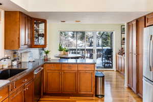 Kitchen featuring tasteful backsplash, light wood-type flooring, appliances with stainless steel finishes, dark stone countertops, and sink