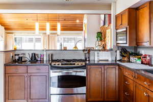 Kitchen featuring stainless steel appliances, pendant lighting, wood ceiling, and decorative backsplash