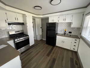 Kitchen with black refrigerator, stainless steel gas stove, sink, and white cabinetry