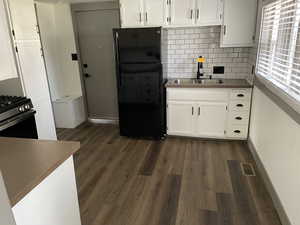 Kitchen featuring white cabinets, sink, dark hardwood / wood-style floors, black fridge, and gas range oven