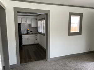 Kitchen featuring white cabinets, decorative backsplash, sink, dark carpet, and crown molding