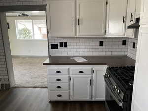 Kitchen with extractor fan, range with gas stovetop, dark wood-type flooring, white cabinetry, and backsplash