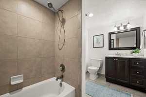 Full bathroom featuring toilet, tiled shower / bath, vanity, tile patterned floors, and a textured ceiling