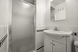 Bathroom with tile walls, an enclosed shower, and vanity