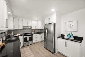 Kitchen featuring backsplash, sink, stainless steel appliances, and white cabinetry