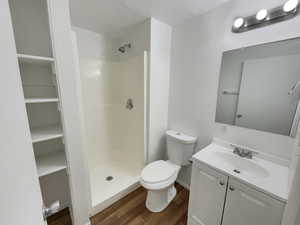 Bathroom featuring toilet, vanity, wood-type flooring, and a shower