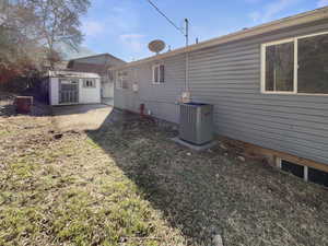 Back of house featuring a yard, a storage shed, and central AC