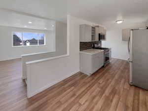 Kitchen with decorative backsplash, gray cabinetry, stainless steel appliances, and light hardwood / wood-style floors