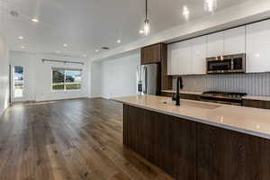 Kitchen with white cabinetry, stainless steel appliances, decorative light fixtures, light stone countertops, and sink