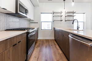 Kitchen with white cabinetry, appliances with stainless steel finishes, decorative backsplash, decorative light fixtures, and sink