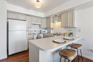 Kitchen with kitchen peninsula, sink, white appliances, and a breakfast bar area