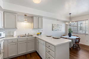 Kitchen featuring pendant lighting, kitchen peninsula, sink, white appliances, and white cabinetry