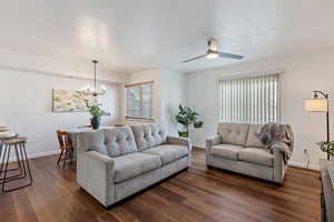 Living room featuring ceiling fan with notable chandelier, dark wood-type flooring, and a textured ceiling