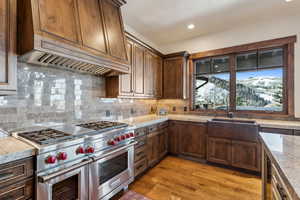 Kitchen featuring decorative backsplash, range with two ovens, light stone countertops, light hardwood / wood-style flooring, and sink