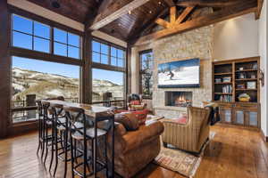 Living room with hardwood / wood-style flooring, a stone fireplace, wooden ceiling, high vaulted ceiling, and beam ceiling