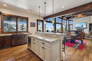 Kitchen with decorative light fixtures, beamed ceiling, sink, light stone counters, and a breakfast bar