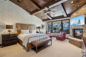 Carpeted bedroom with ceiling fan, vaulted ceiling, a fireplace, and wood ceiling