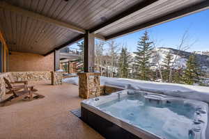 Snow covered patio featuring a mountain view and a hot tub