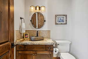 Bathroom featuring toilet, vanity, and tasteful backsplash