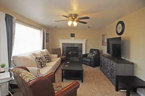 Carpeted living room with ceiling fan and a tiled fireplace