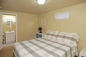 Bedroom with ensuite bathroom, light carpet, sink, and a textured ceiling