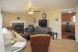 Carpeted living room featuring a textured ceiling, ceiling fan, and a fireplace