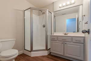 Bathroom with an enclosed shower, vanity, toilet, and hardwood / wood-style flooring