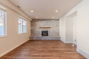 Unfurnished living room featuring plenty of natural light, wood-type flooring, and a stone fireplace