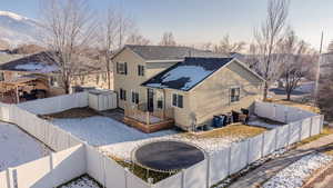 Snow covered rear of property featuring a trampoline and a storage unit