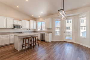 Kitchen featuring white cabinets, a kitchen island, decorative light fixtures, stainless steel appliances, and dark hardwood / wood-style floors