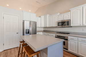 Kitchen featuring white cabinets, appliances with stainless steel finishes, a center island, vaulted ceiling, and a breakfast bar