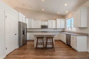 Kitchen featuring white cabinetry, a breakfast bar area, appliances with stainless steel finishes, dark wood-type flooring, and a kitchen island