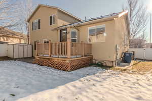 Snow covered back of property featuring a wooden deck and a shed