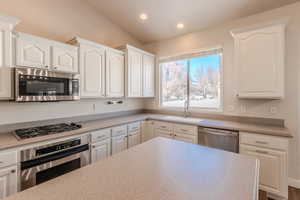 Kitchen featuring sink, white cabinets, appliances with stainless steel finishes, and lofted ceiling