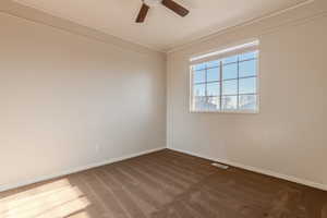 Unfurnished room with ceiling fan, crown molding, and dark colored carpet